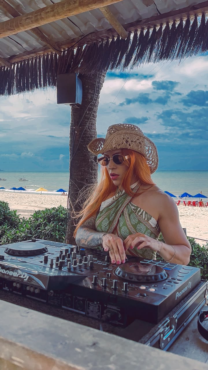 DJ Nadia Brito tocando em uma cabine de praia à beira-mar